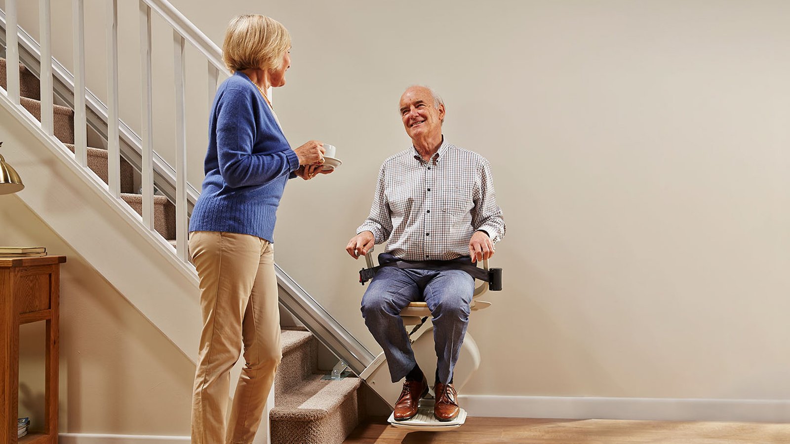 An older couple at home beside a straight stairlift