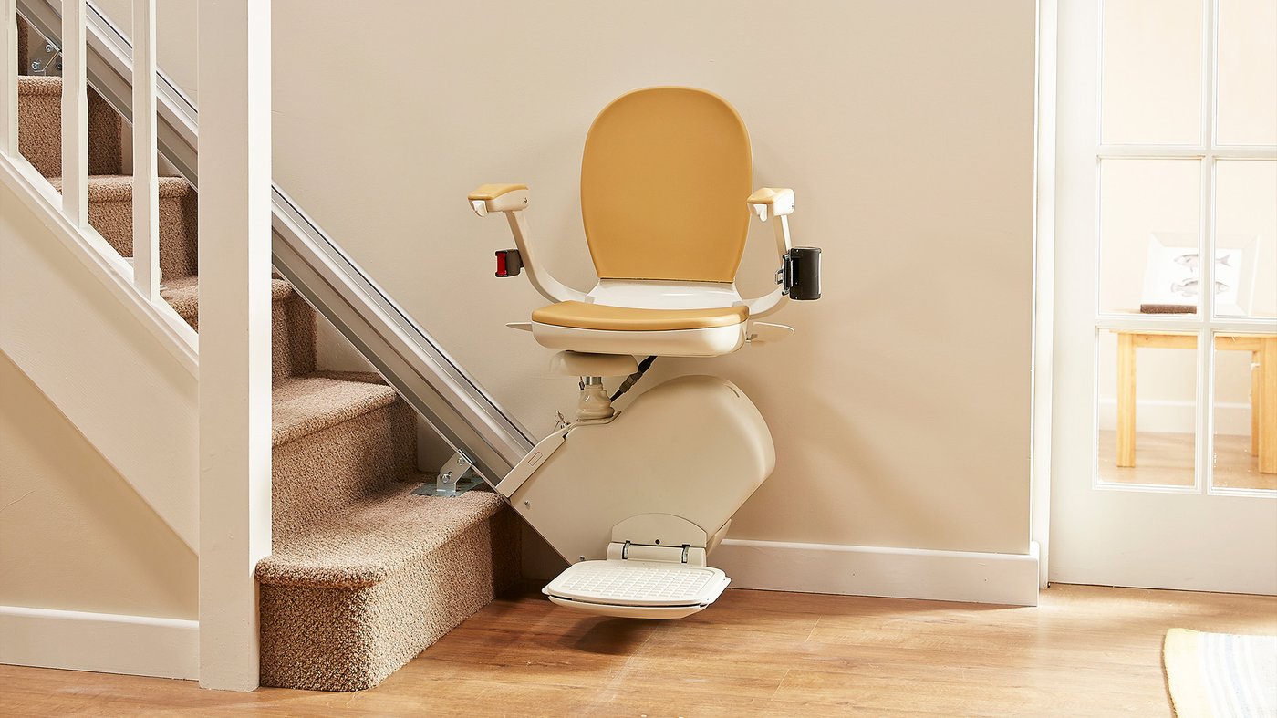 A straight stairlift parked at the bottom of a carpeted staircase
