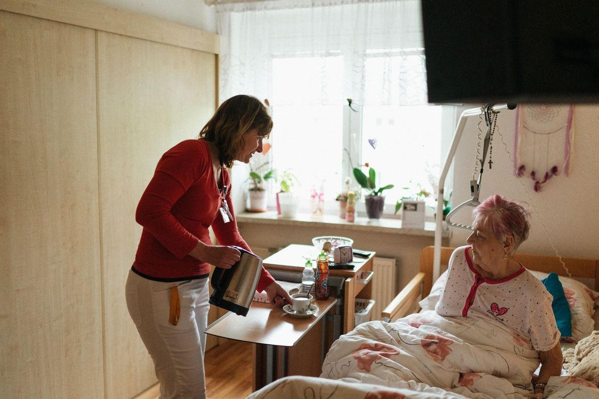 A carer pouring tea for an older woman sitting up in bed at home
