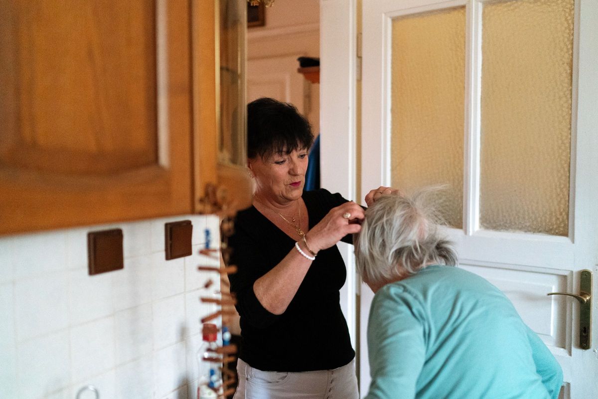 A carer gently doing an older woman's hair in the hallway of her home