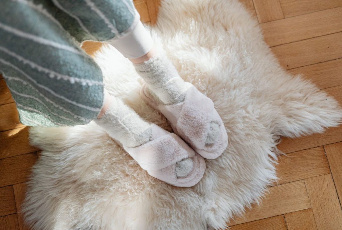 Feet in soft socks and slippers standing on a sheepskin rug on a wooden floor