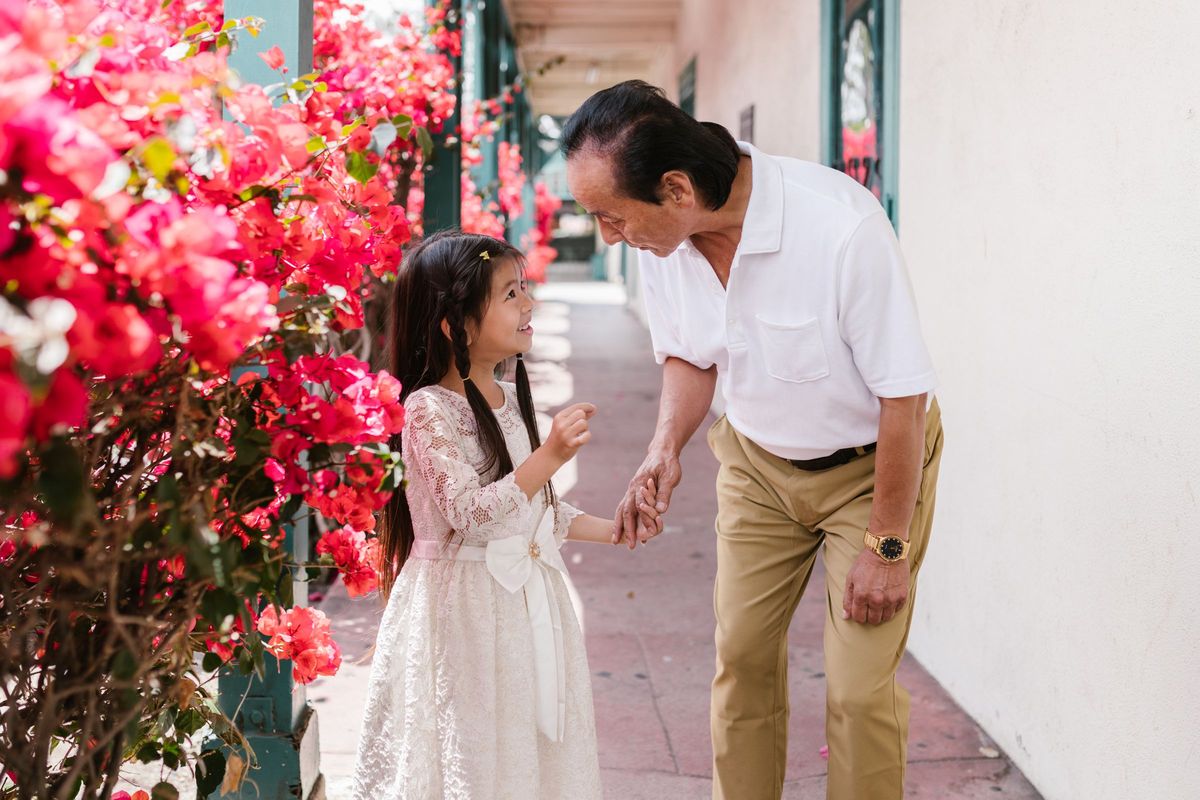 An older man holding hands with his young granddaughter on a walk past flowering shrubs