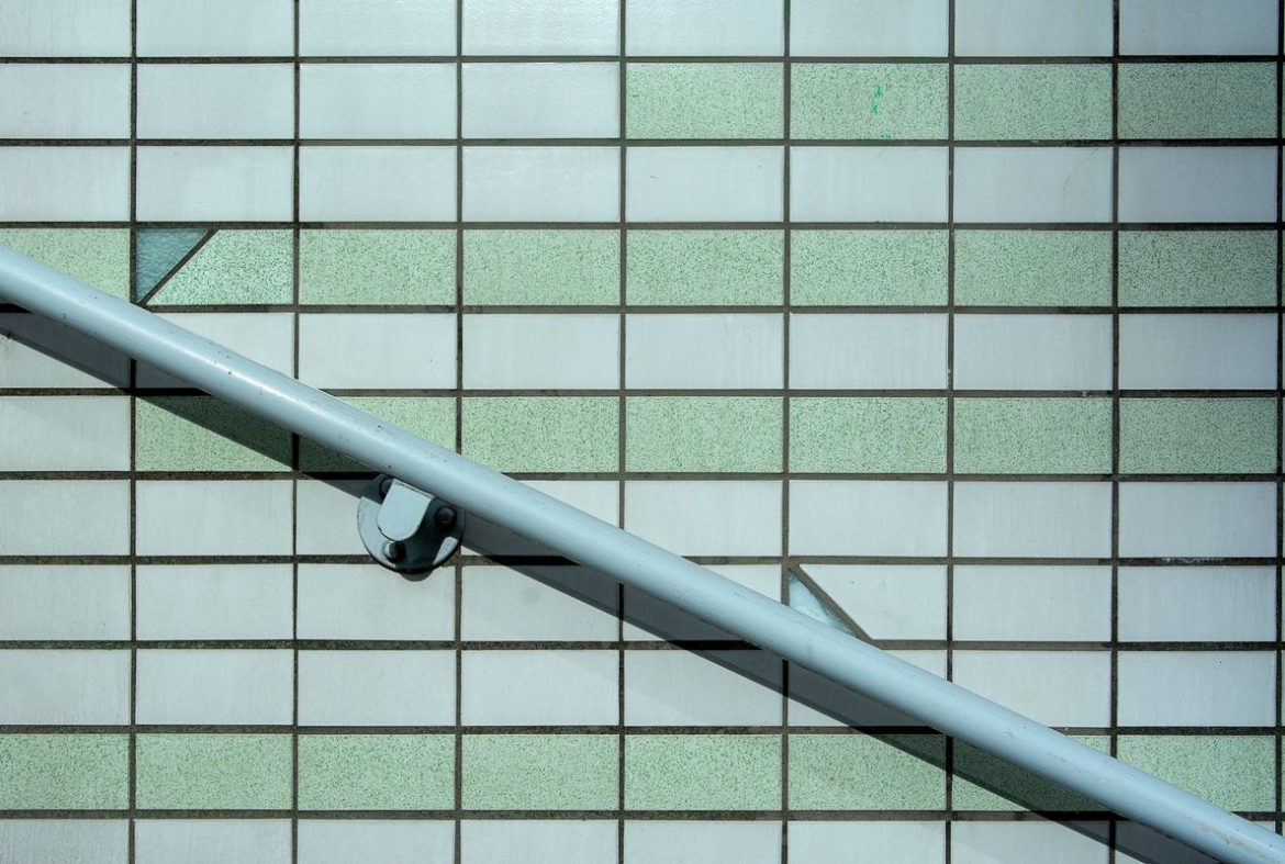 A pale grey handrail fixed to a bright tiled wall