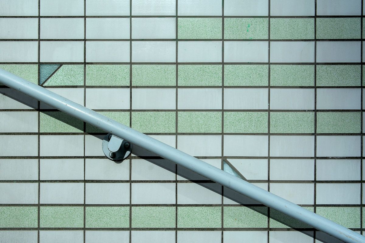 A pale grey handrail fixed to a bright tiled wall