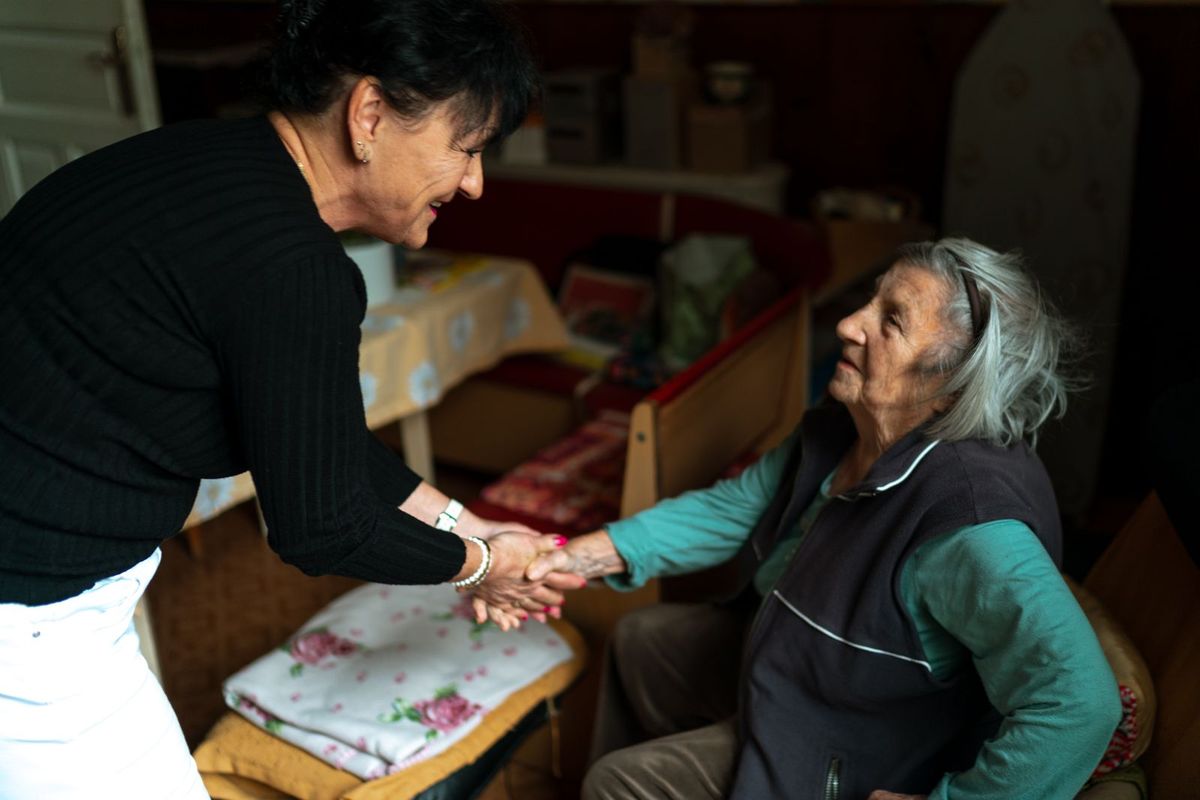 A younger woman and an older woman holding hands and smiling in a living room