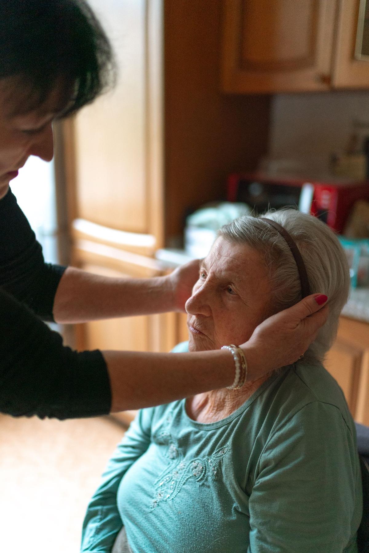 A younger woman gently holding an older womanâ€™s face in a kitchen at home