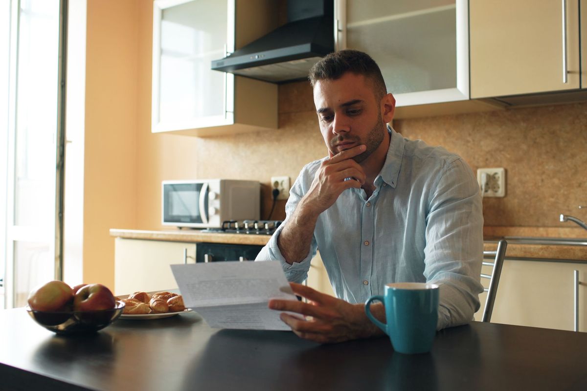 A man reading a letter at a kitchen table beside a mug