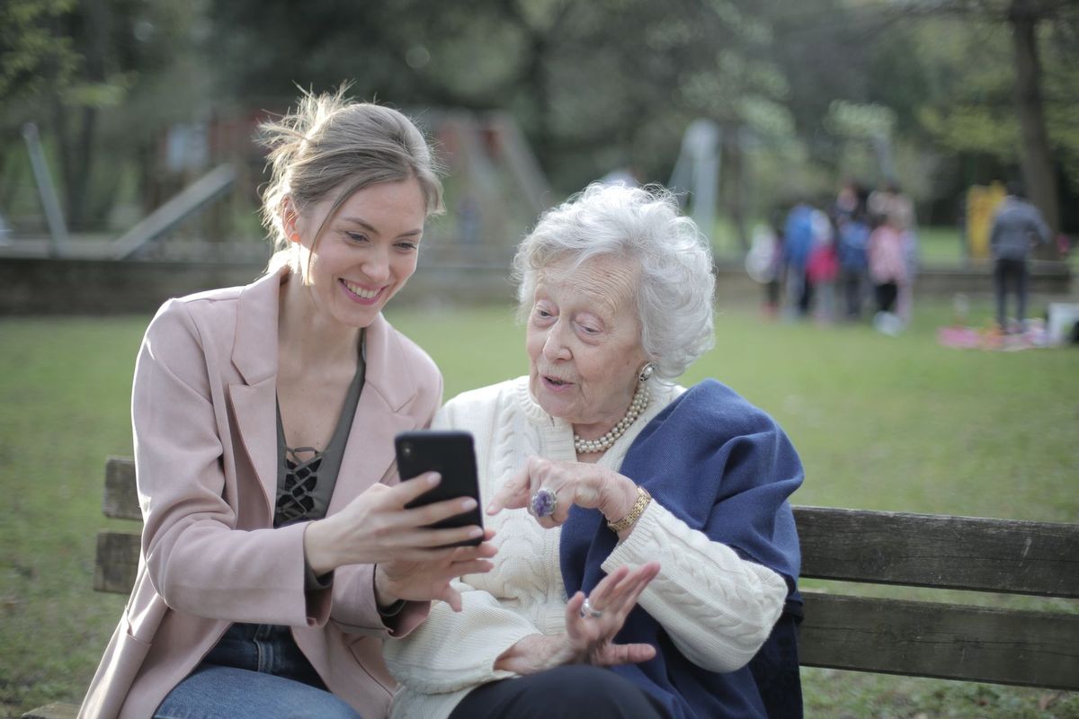 An older woman and a younger woman looking at a smartphone together on a park bench
