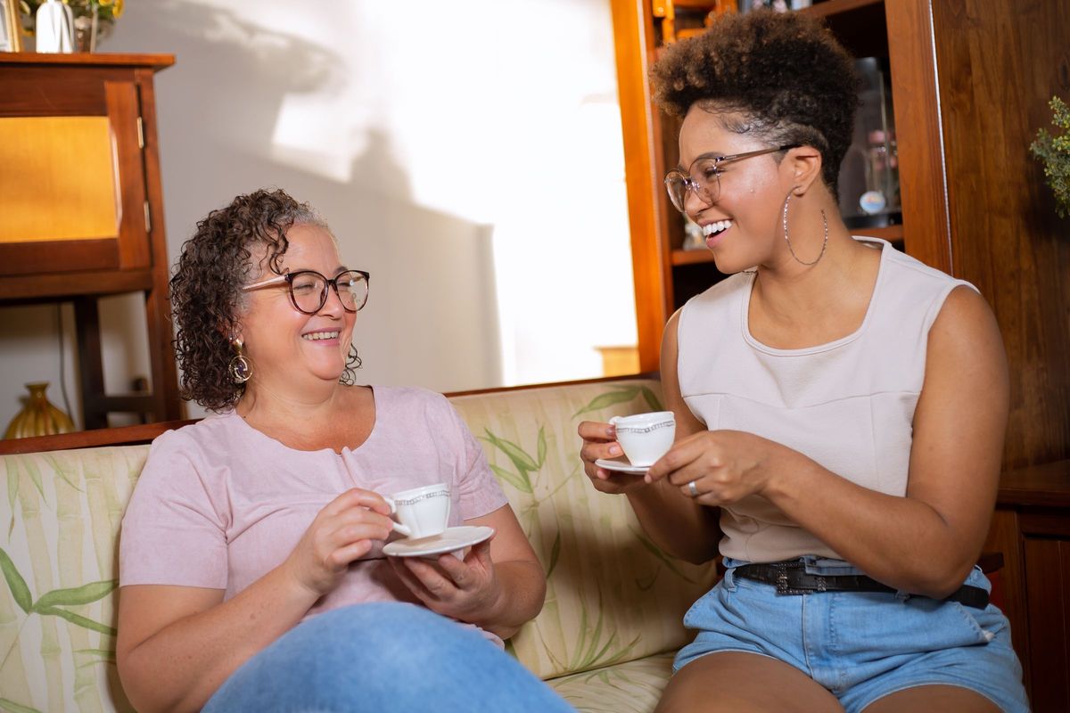 An older woman and a younger woman sharing a cup of tea on a sofa at home