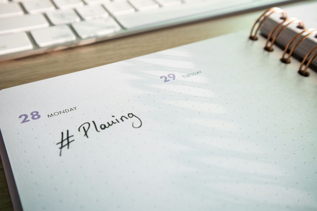 An open planner and notepad on a desk beside a keyboard