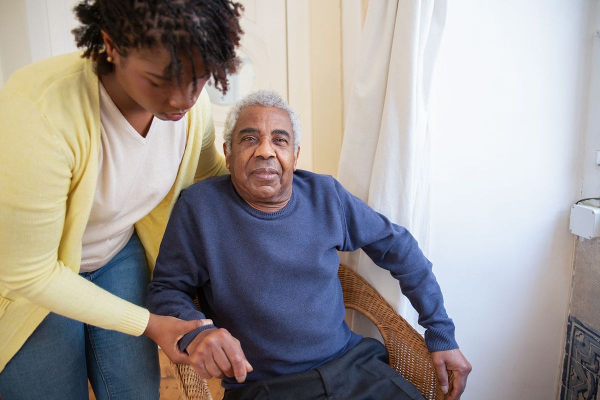 A woman assisting an older man as they sit together at home